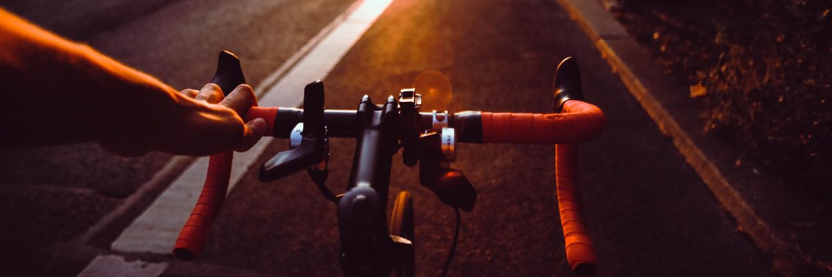 biciklikormány és az azt fogó kéz a naplementében az úton