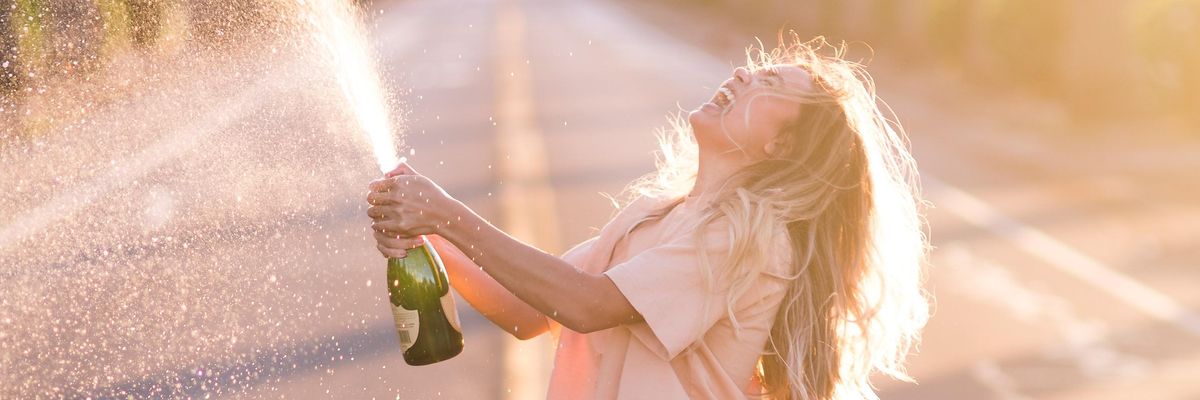 boldog nő spriccelve pezsgőt bont az út közepén állva