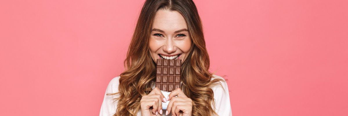 csokoládét tart a szájához mosolyogva egy nő