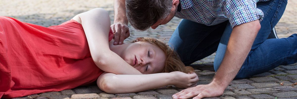 egy férfi ellenőrzi egy földön fekvő nő pulzusát