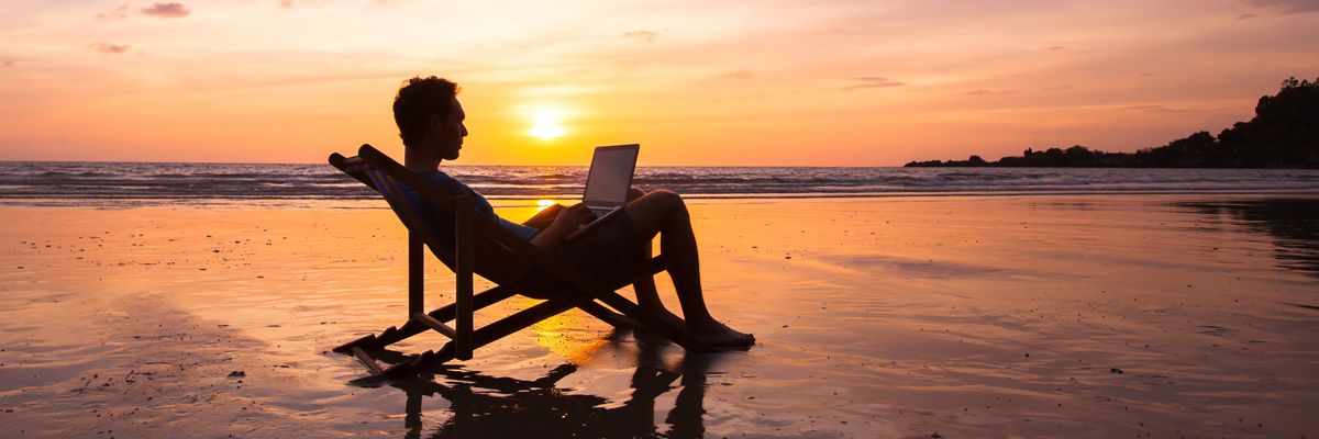 egy férfi laptopozik a tengerparton a naplementében