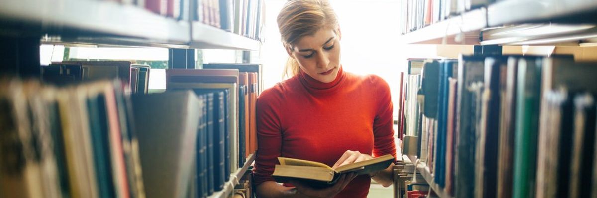 egy fiatal nő olvas a könyvtárban a sorok között állva
