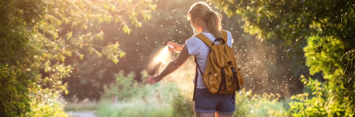 egy hátizsákos nő szúnyogrisztóval fújja magát a napfényben a természetben