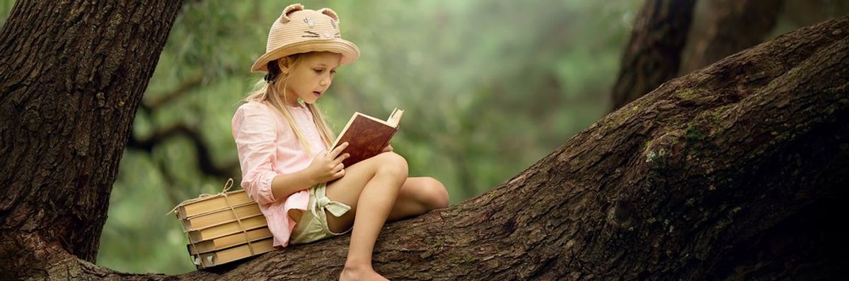 egy kislány olvas a fán ülve, szalmakalapban