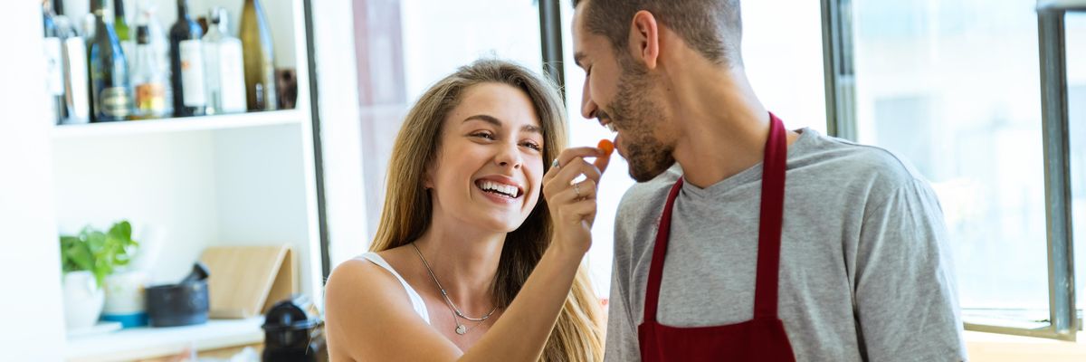 egy nő a férfi szájába ad egy darab ételt miközben közösen főznek