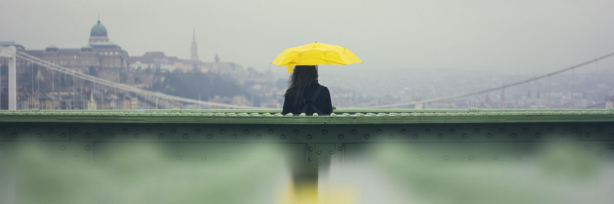egy nő áll sárga esernyővel a Szabadság Hídon