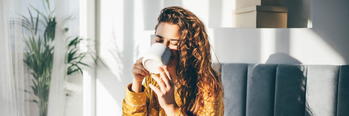 egy nő az ágyában issza a reggeli kávéját