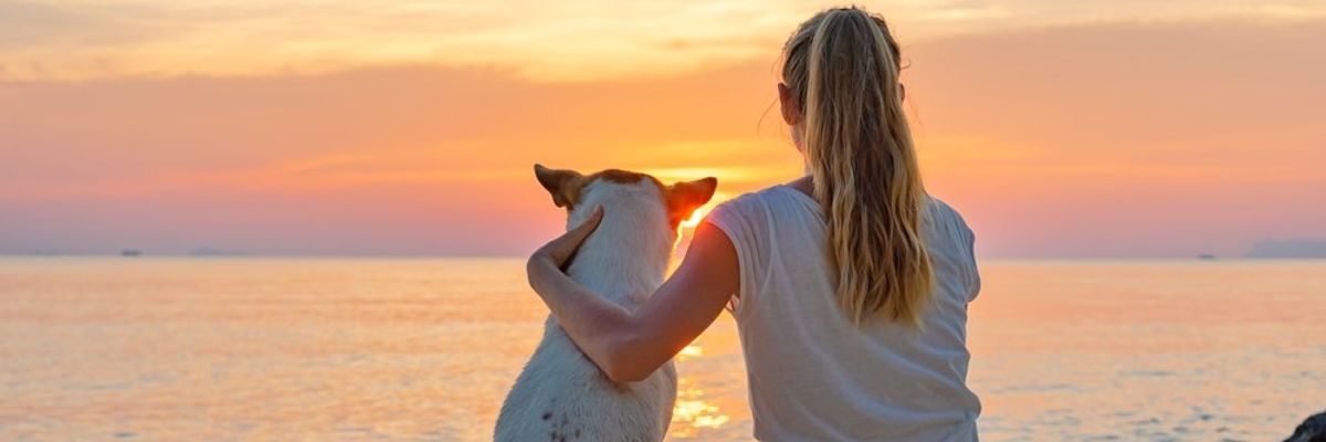 egy nő ül a kutyájával a naplementében a vízparton