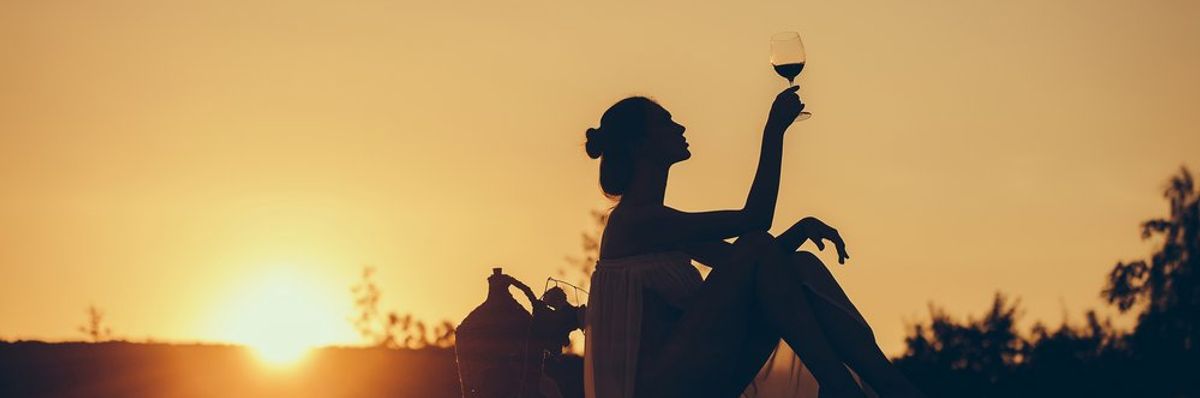 egy pohár bort tart a kezében egy nő a természetben