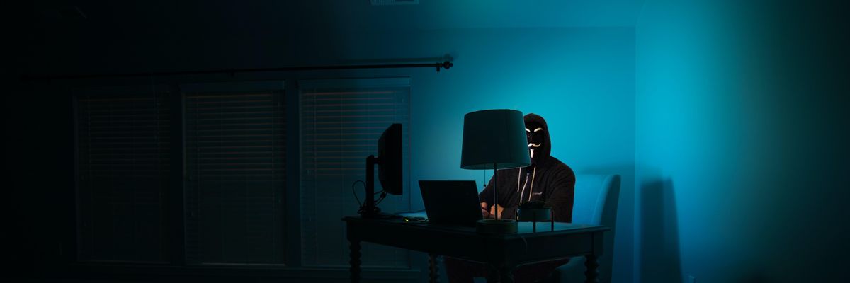 egy sötét szobában egy álarcos hacker ül egy számítógép előtt