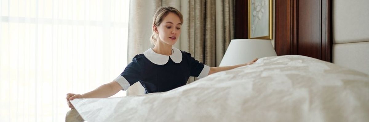 egy szobalány beveti az új ágyneművel az ágyat egy szállodában