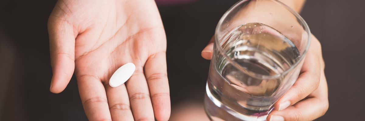 Egy tablettát és egy pohár vizet tartó kéz