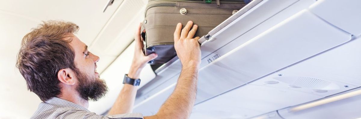 egy utas felteszi a bőröndjét a repülőn a rekeszbe