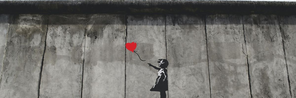 fekete fehér kislány piros szív alakú lufit enged el szállni a levegőben rajz egy szürke falon