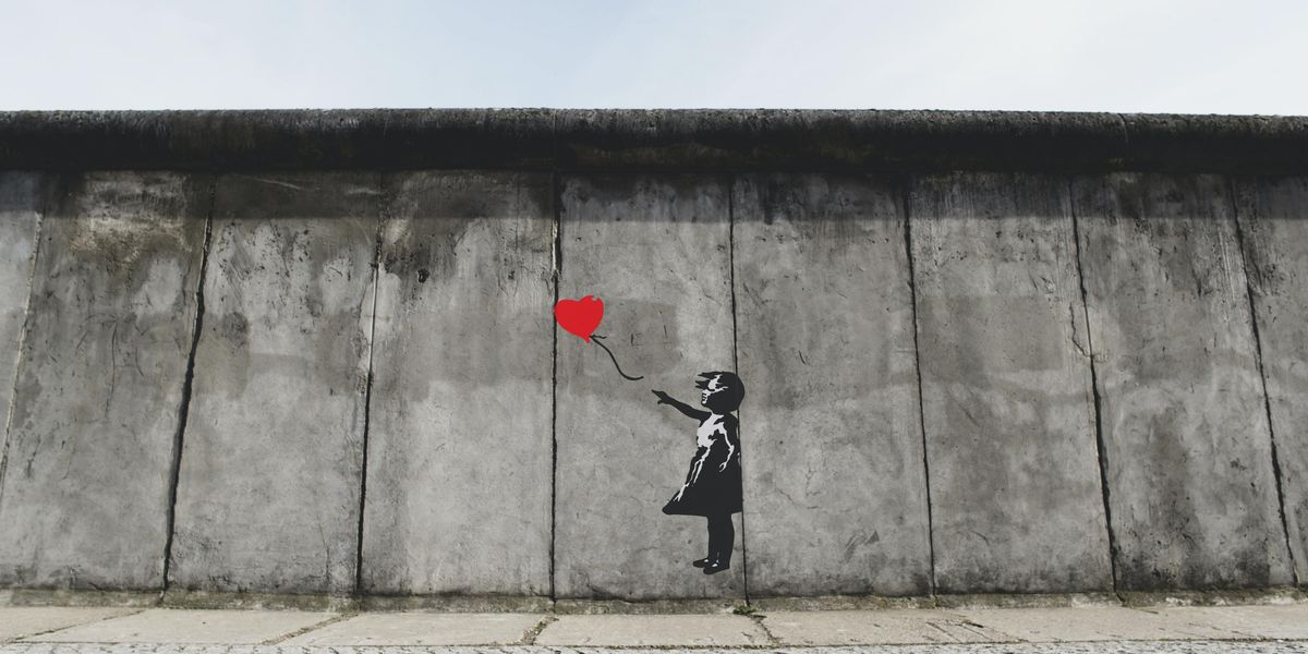 fekete fehér kislány piros szív alakú lufit enged el szállni a levegőben rajz egy szürke falon