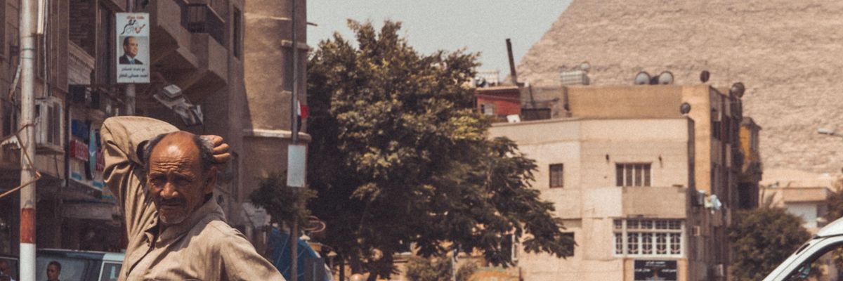 férfi áll Kairóban az utcán, mögötte piramis