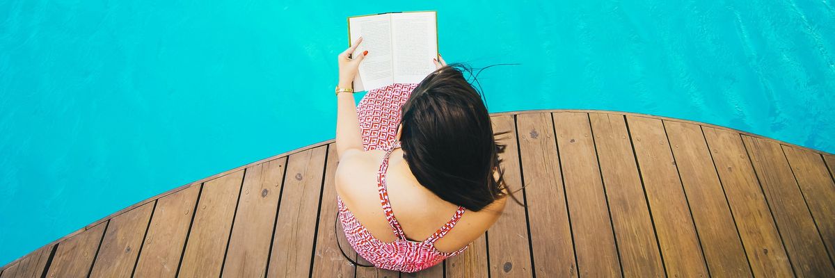 Fiatal nő egy medence partján ül a stégen, és egy könyvet olvas