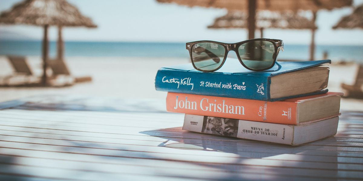 Három könyv és egy napszemöveg a homokos tengerparton