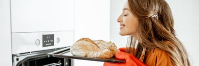 egy nő friss kenyeret vesz ki a sütőből