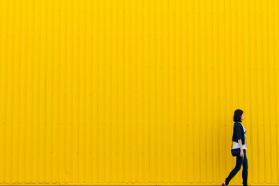 Nő sétál egy sárga fal előtt