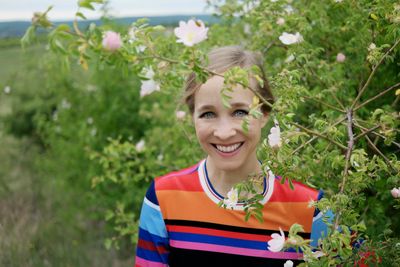 Harcsa Veronika énekesnő egy faág mögött, színes ruhában
