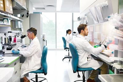 orvosok kutatók széken ülnek mikroszkóppal végeznek vizsgálatokat fehér köpenyben