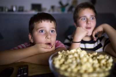 gyerekek tévét néznek csíkos pólóban meglepett fej popcorn az asztalon előttük