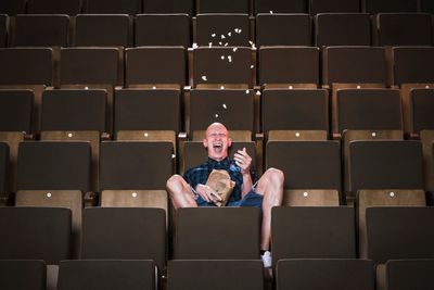 kopasz férfi moziban ül popcornnal a kezében nevet kockás ing rövidnadrág fehér sportcipő nézőtér lelátó székek