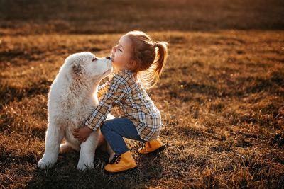 fehér szőrű kutyát ölel egy kockás inges szőke kislány a mezőn