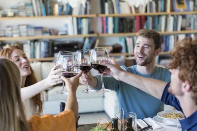 baráti összejövetel két férfi és nő egy étkezőasztal fölött koccint vörösborral és esznek egy amerikai konyhás nappali étkezőben szexi pasik csinos lányok