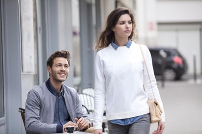 szexi izmos jóképű férfi egy fehér pulóverben sétáló nő után néz az utcán egy kávézó teraszán