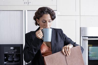 sietésben lévő nő reggel egy bögre kávéval és egy aktatáskával a kezében gyűrű az ujján női szmokingban kisminkelve a konyhában