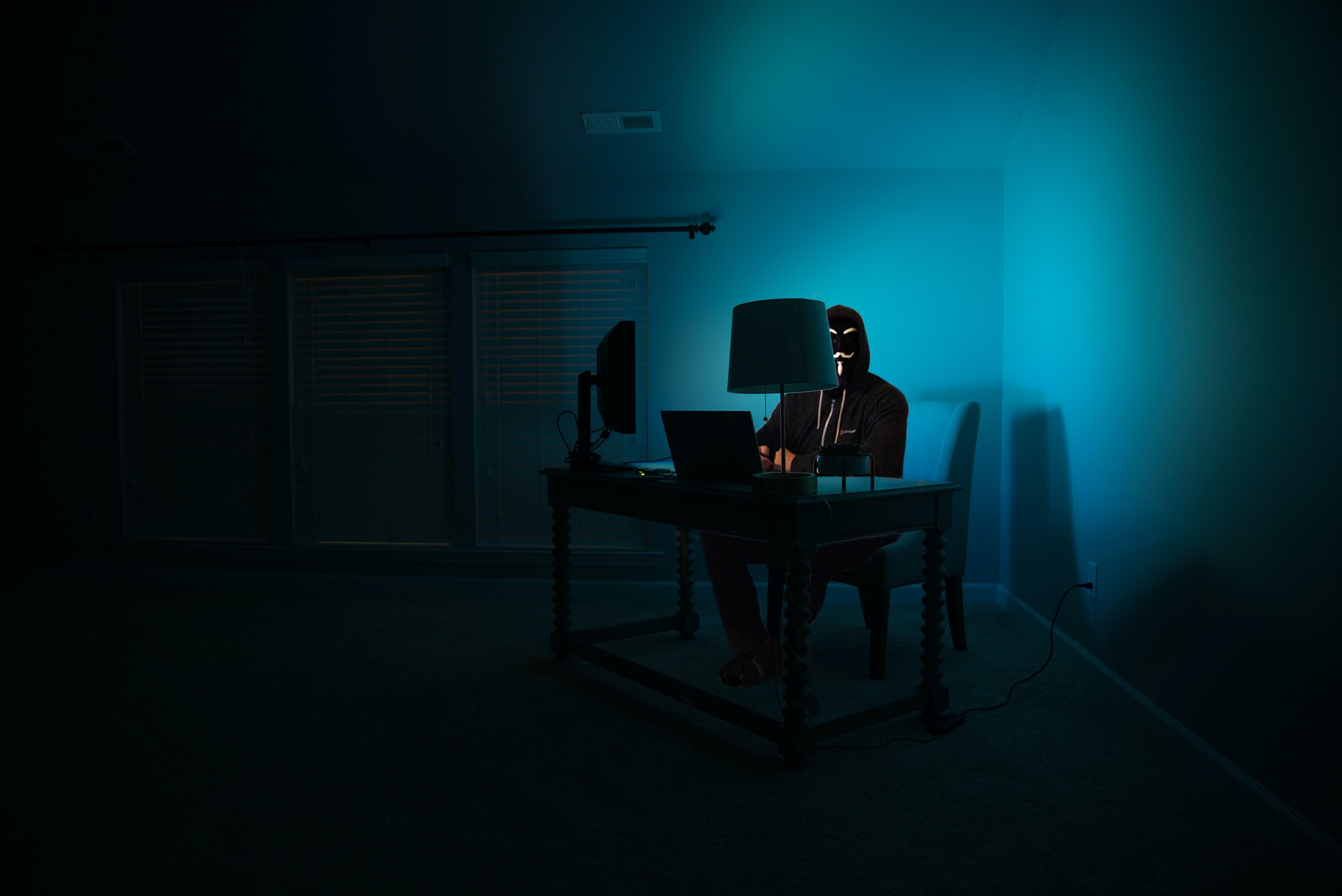 egy sötét szobában egy álarcos hacker ül egy számítógép előtt