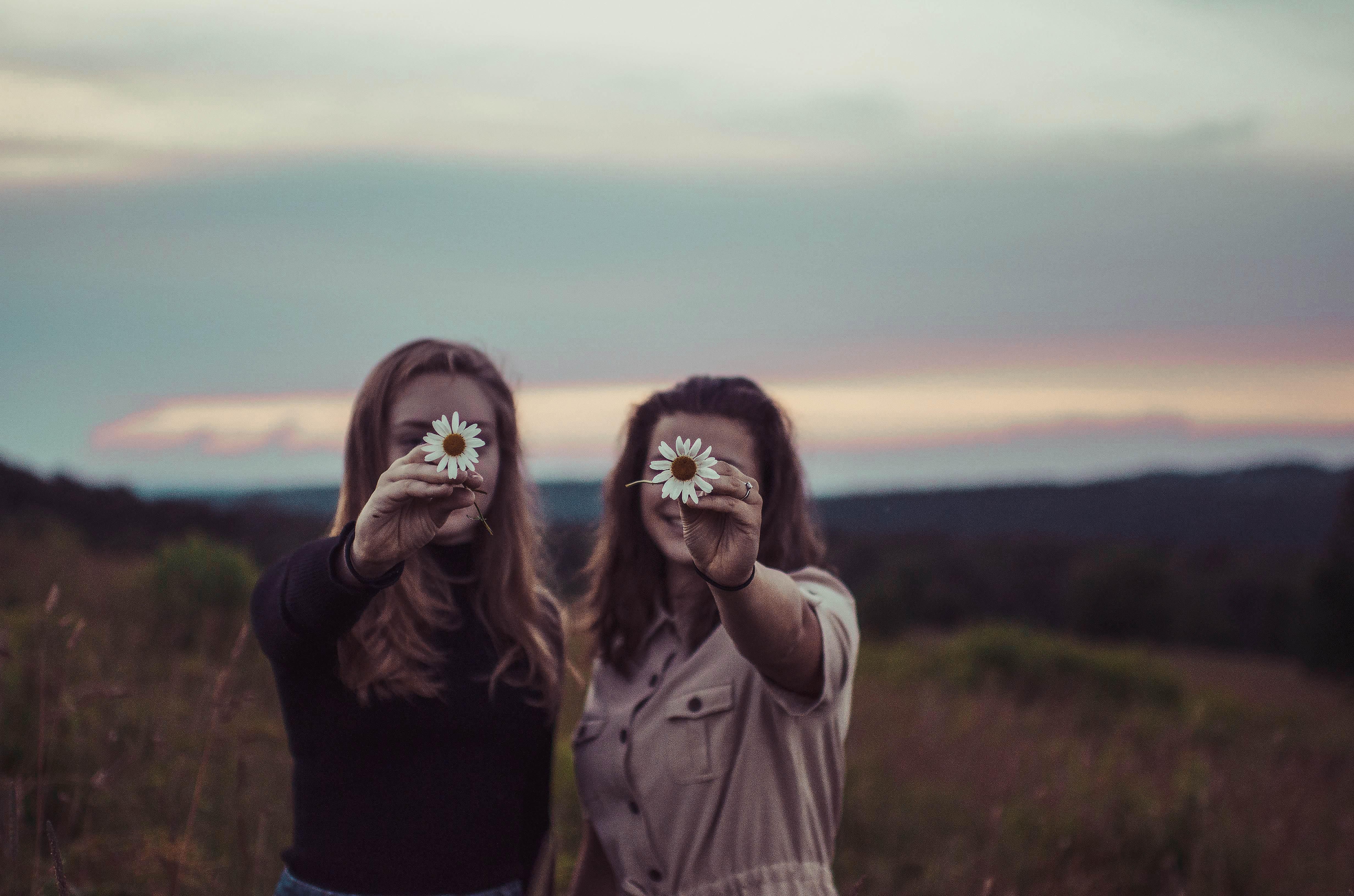 két lány egy réten, virágot tartva az arcuk elé