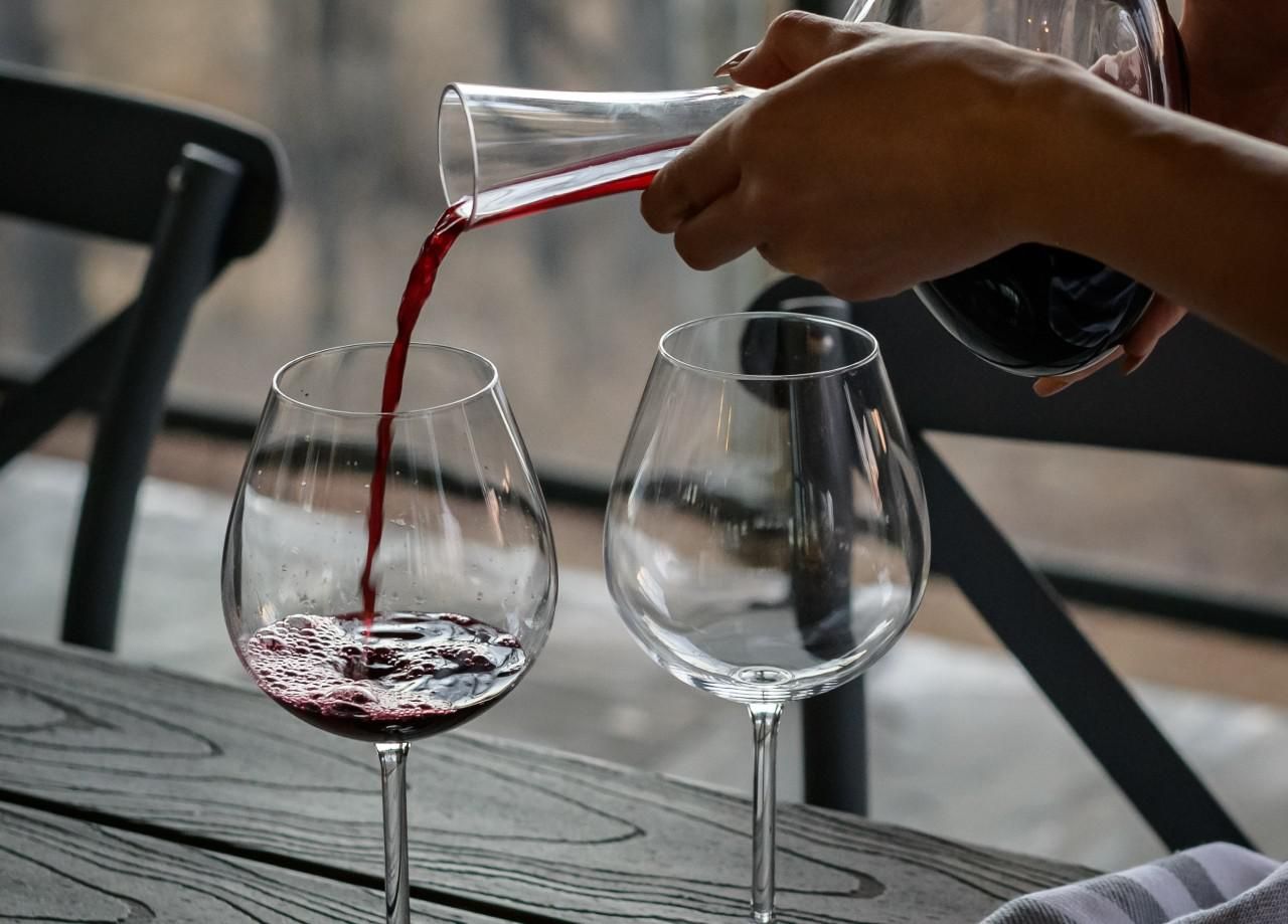 egy női kéz vörösbort tölt ki egy pohárba