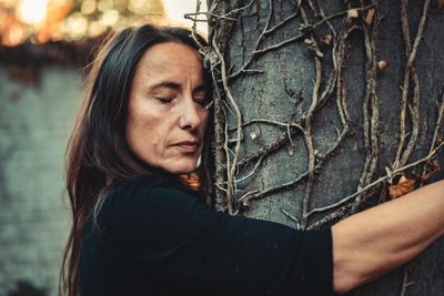 woman in black shirt leaning on brown tree