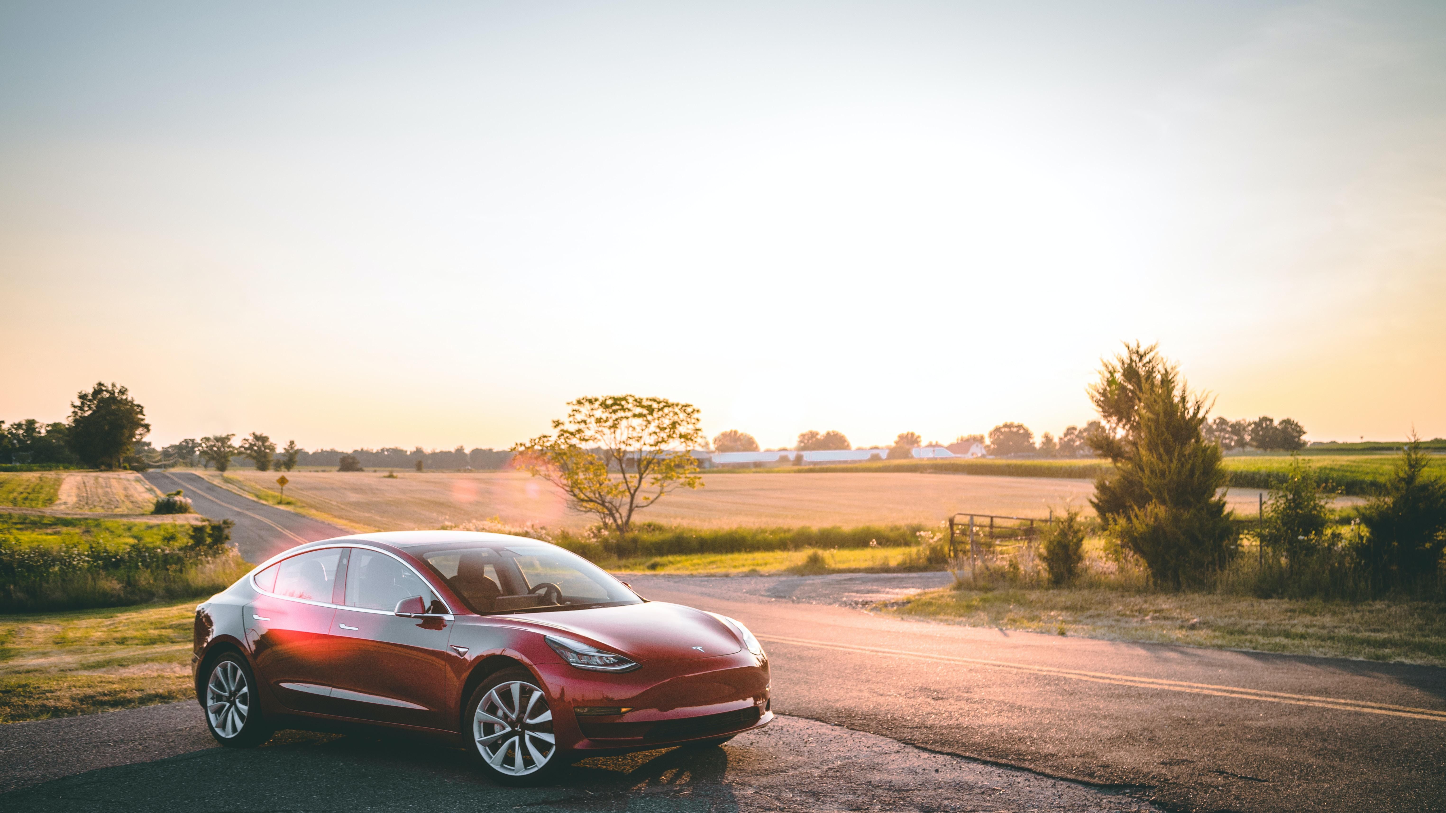 Egy piros Tesla Modell 3-as a naplementében.