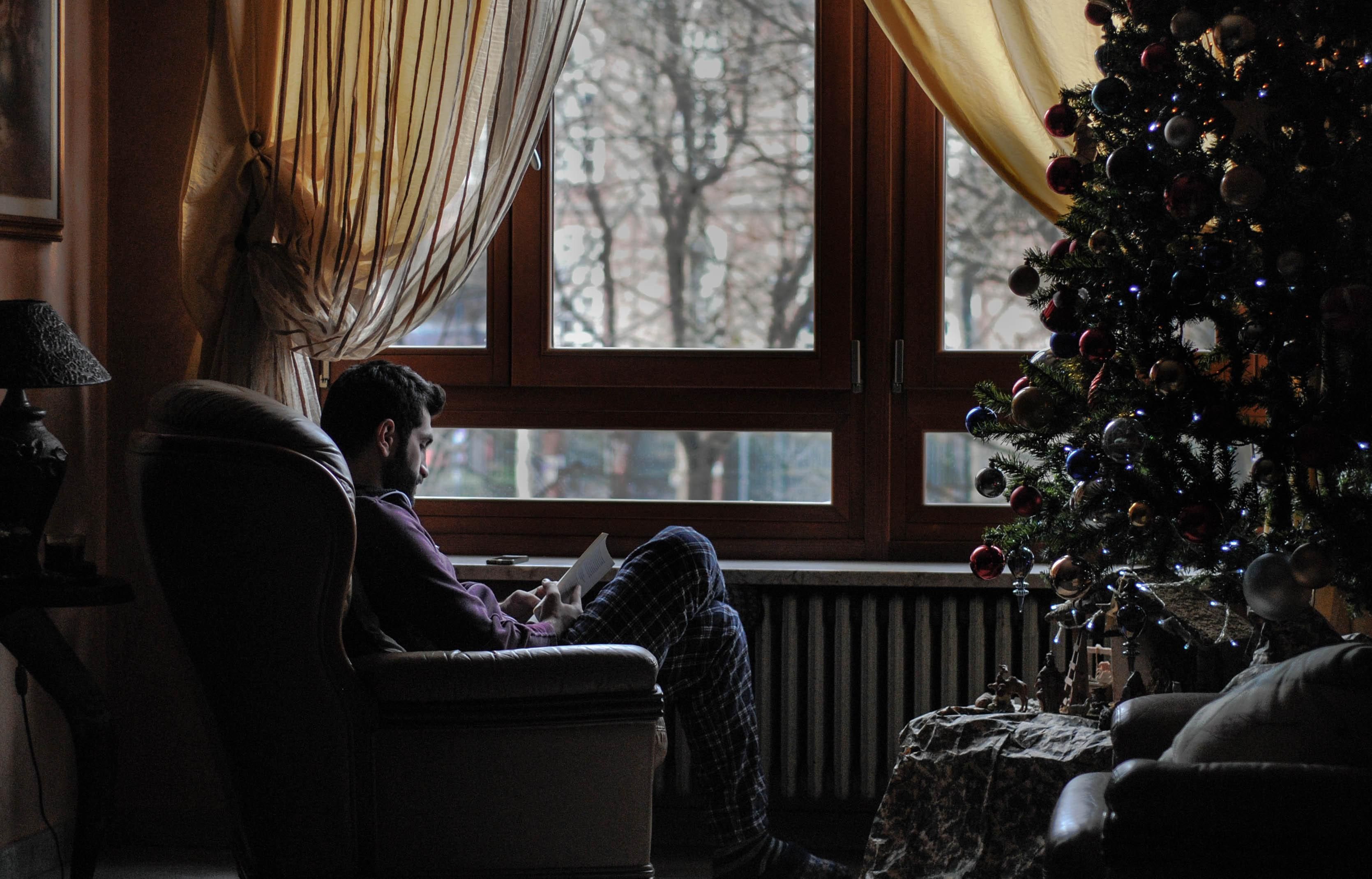 Férfi ül a fotelban és olvas, mellette karácsonyfa