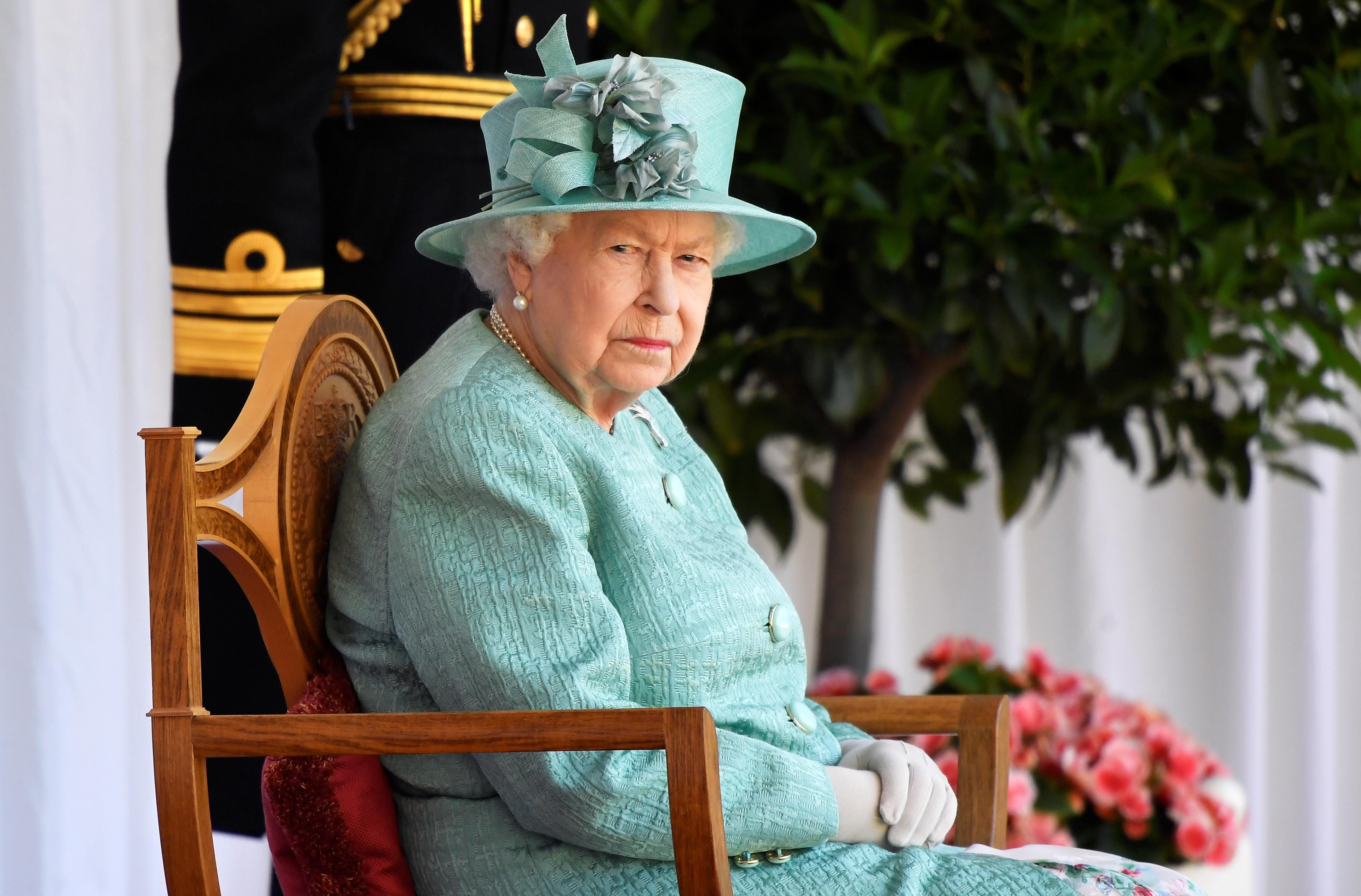 A királynő zöld ruhában ül egy széken.