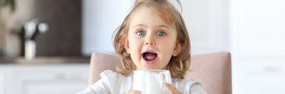 kislány tejes szájjal egy tejes poharat tart a kezében