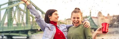 két fiatal lány konfettit szór és italt tart a kezében Budapesten az utcán