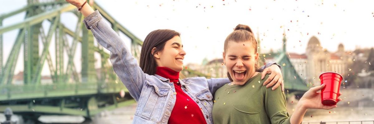 két fiatal lány konfettit szór és italt tart a kezében Budapesten az utcán