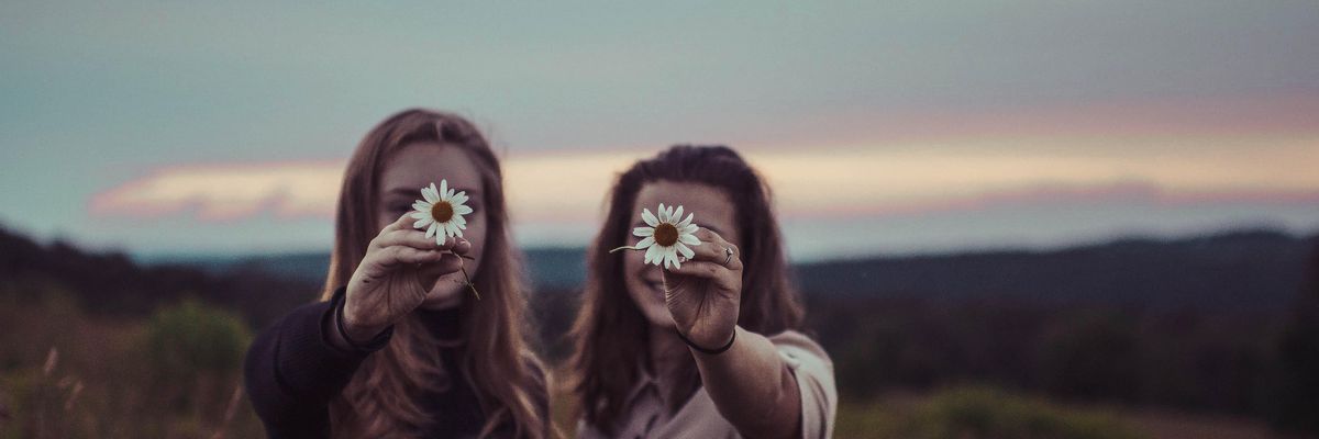két lány egy réten, virágot tartva az arcuk elé