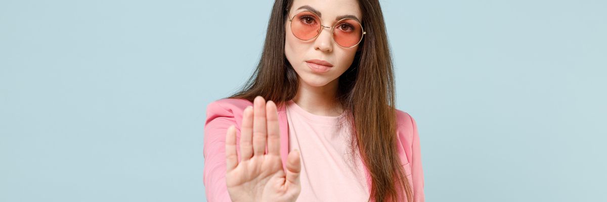 kezével elutasítást mutató fiatal nő rózsaszín blézerben, piros kerek napszemüvegben