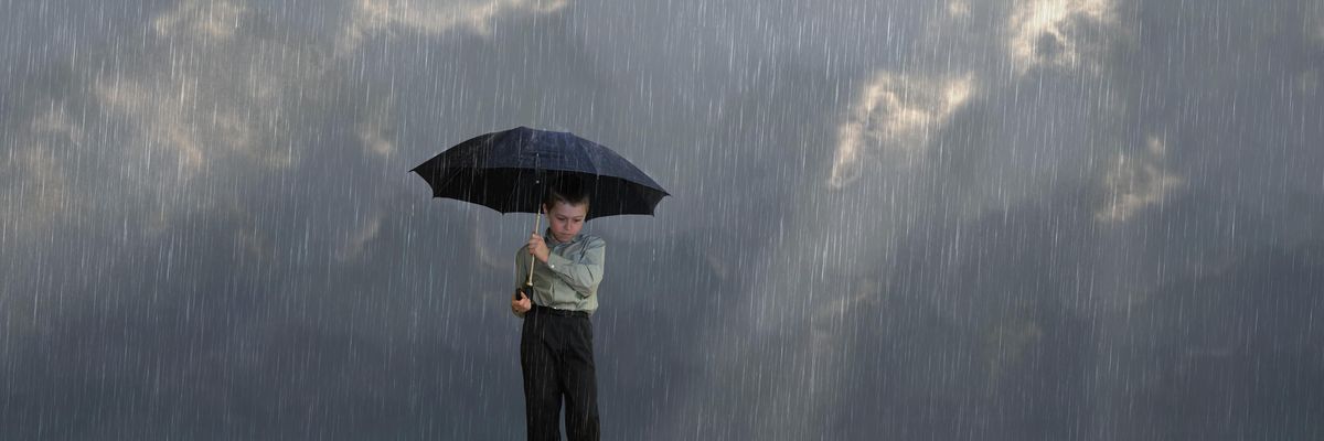 kisfiú esernyővel áll egy sziklán
