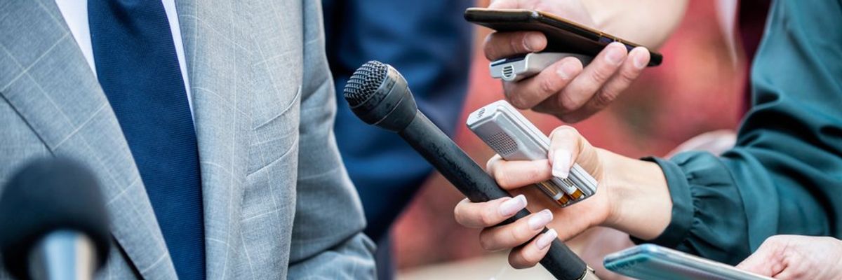 mikrofont, diktafonokat és telefonokat tartanak egy öltönyös ember elé az újságíók