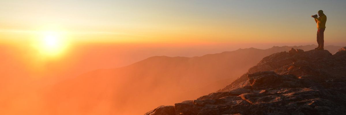 napfelkelte a hegyekben fotós férfi fotóz képet készít egy sziklán állva fényképezőgéppel