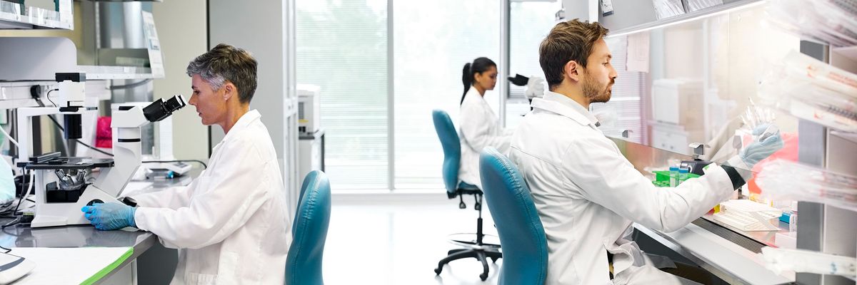 orvosok kutatók széken ülnek mikroszkóppal végeznek vizsgálatokat fehér köpenyben