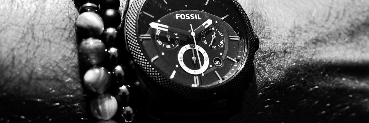 person wearing round Fossil chronograph watch with link band displaying 01:47 time
