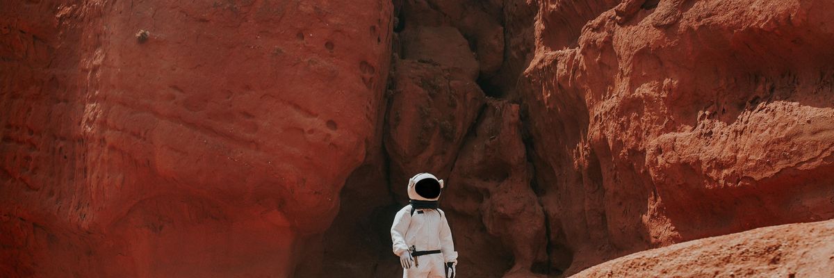 photography of astronaut standing beside rock formation during daytime